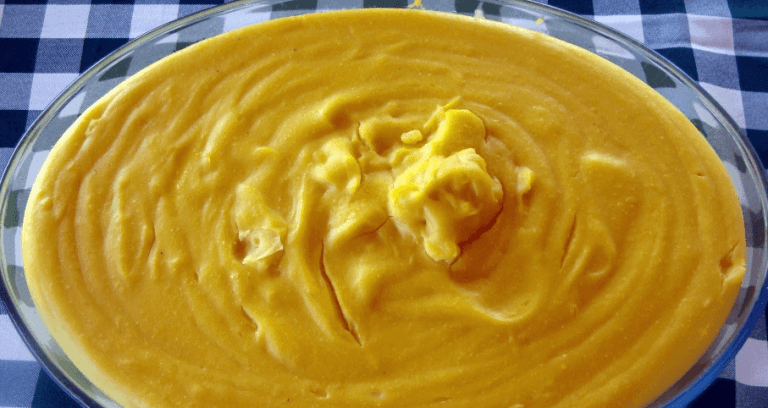 Tigela de angu amarelo cremoso servido sobre uma toalha de mesa xadrez azul e branca.