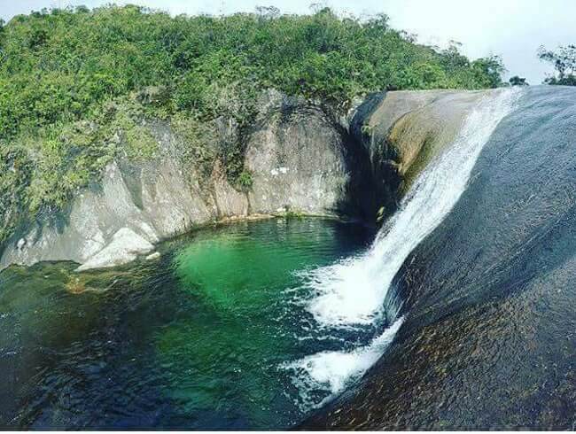 Cachoeira de águas cristalinas caindo em uma piscina natural rodeada por rochas e vegetação densa na Serra do Caparaó.